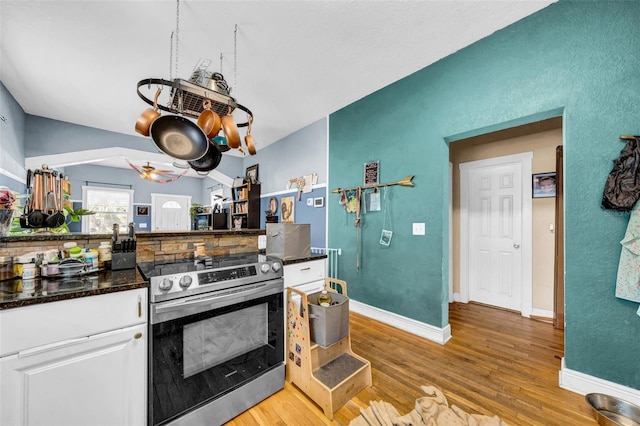 kitchen with light wood finished floors, dark countertops, electric range, white cabinets, and baseboards