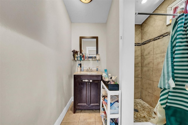 bathroom featuring vanity, baseboards, tiled shower, and tile patterned floors