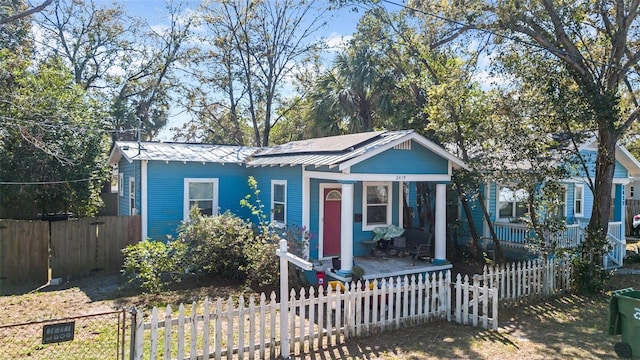 bungalow-style house featuring metal roof, solar panels, a porch, and a fenced front yard