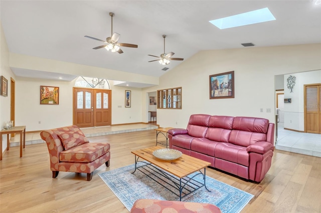 living room featuring visible vents, ceiling fan, light wood finished floors, and vaulted ceiling with skylight