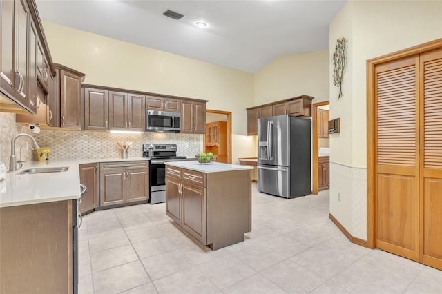 kitchen featuring decorative backsplash, appliances with stainless steel finishes, light countertops, a kitchen island, and a sink