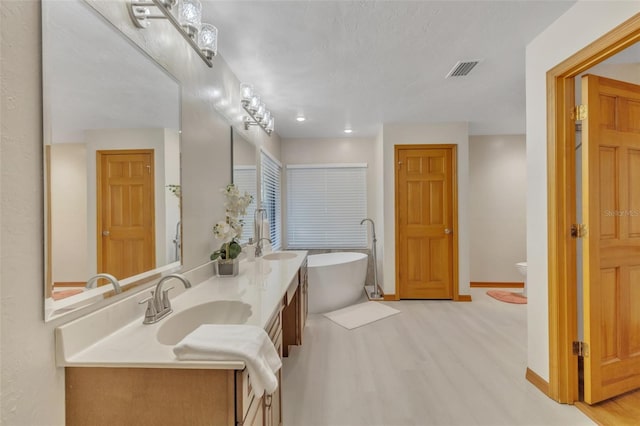 full bathroom featuring wood finished floors, a freestanding bath, double vanity, a sink, and visible vents