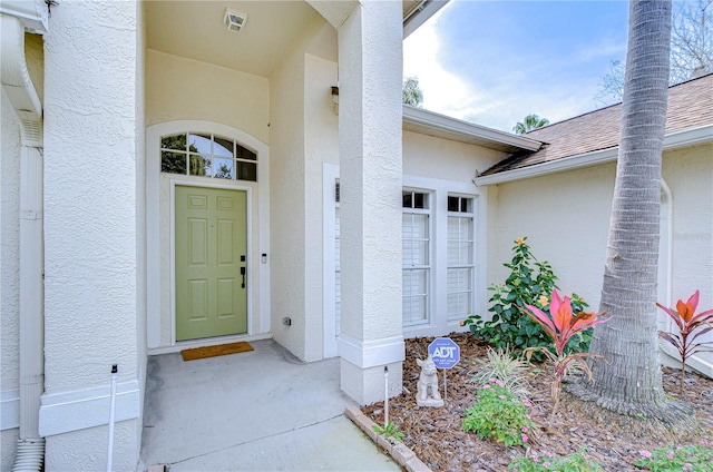 doorway to property featuring roof with shingles, visible vents, and stucco siding