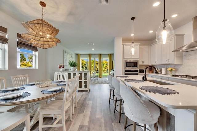 kitchen with backsplash, appliances with stainless steel finishes, white cabinets, a sink, and wall chimney range hood