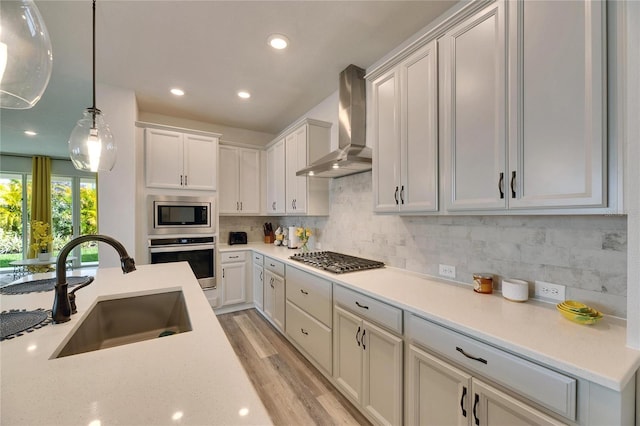 kitchen with tasteful backsplash, appliances with stainless steel finishes, light wood-style floors, a sink, and wall chimney exhaust hood