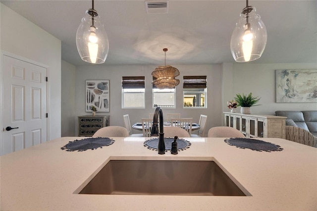 kitchen with visible vents, open floor plan, hanging light fixtures, light countertops, and a sink