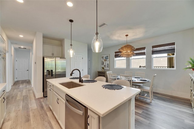 kitchen with light wood finished floors, stainless steel appliances, visible vents, a kitchen island with sink, and a sink