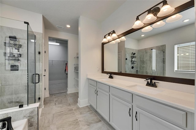 bathroom featuring double vanity, a shower stall, a spacious closet, and a sink