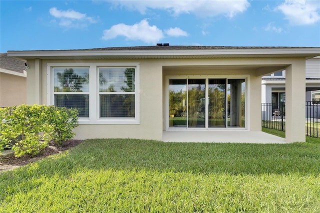 rear view of house with a lawn, fence, and stucco siding