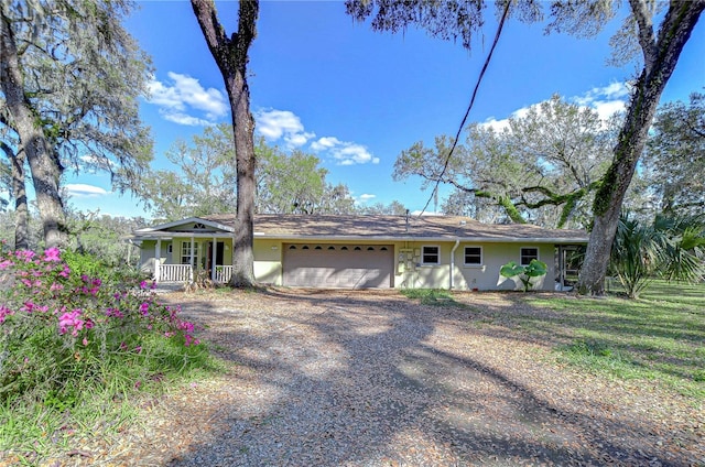 single story home featuring an attached garage, a porch, gravel driveway, and stucco siding