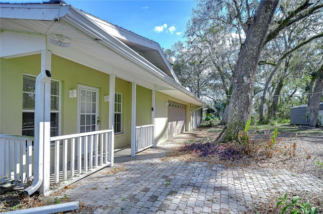 view of side of home with an attached garage, covered porch, decorative driveway, and stucco siding