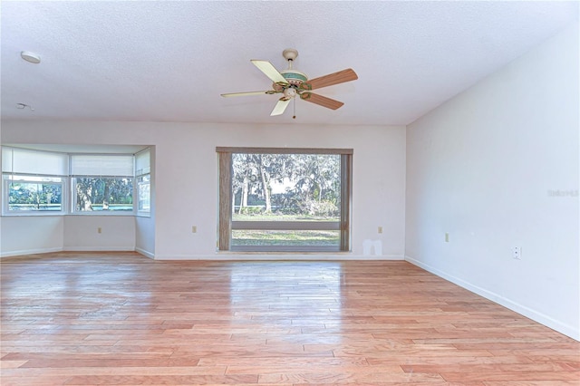 spare room featuring a textured ceiling, ceiling fan, light wood-type flooring, and baseboards