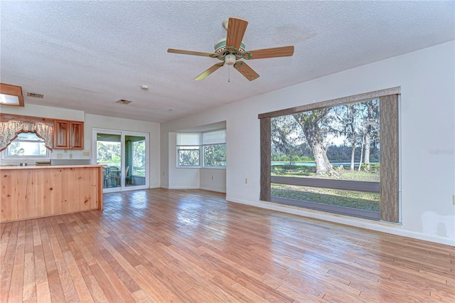 unfurnished living room with ceiling fan, a textured ceiling, light wood-style flooring, visible vents, and baseboards