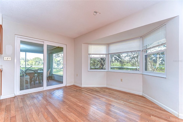 spare room featuring light wood-style floors, a textured ceiling, and baseboards