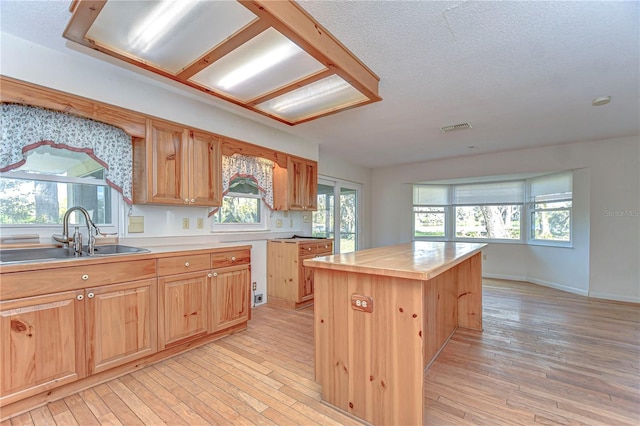 kitchen with light wood-type flooring, visible vents, a sink, and a center island