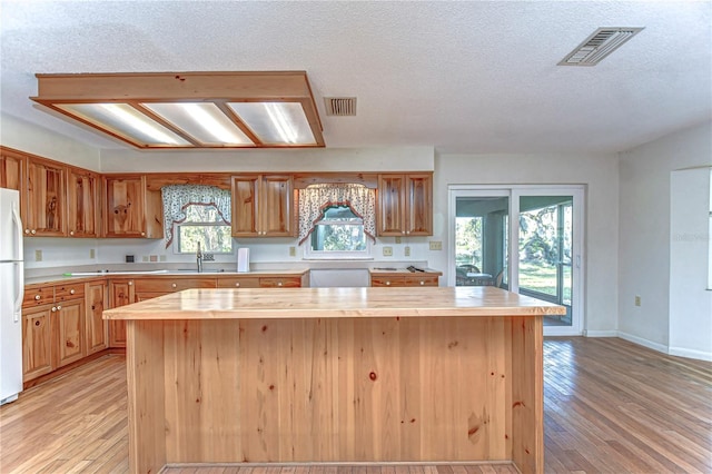 kitchen with light wood-style flooring, visible vents, a sink, and freestanding refrigerator