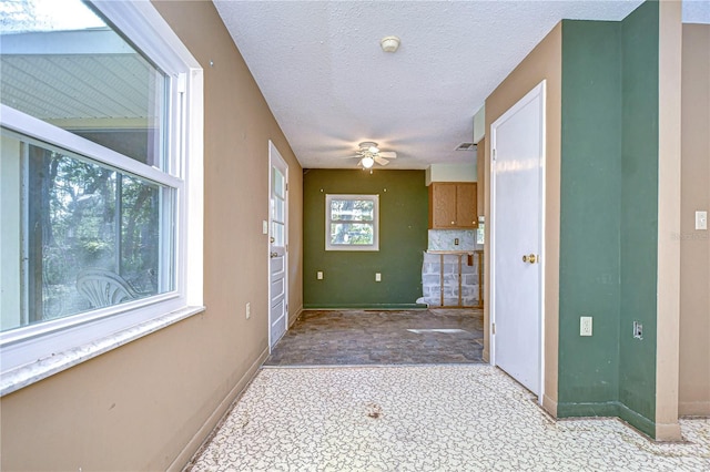 interior space featuring a textured ceiling, a ceiling fan, and baseboards