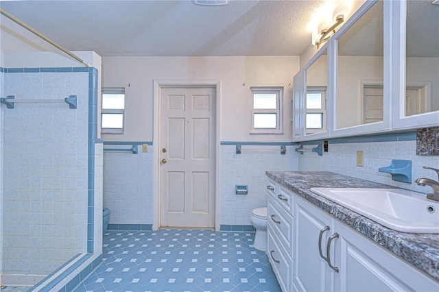 full bathroom featuring a textured ceiling, toilet, vanity, tile walls, and a shower stall