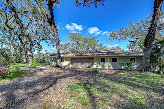 ranch-style home featuring dirt driveway, an attached garage, and stucco siding