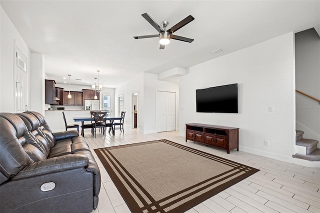 living room featuring stairs, recessed lighting, light wood-style flooring, baseboards, and ceiling fan with notable chandelier