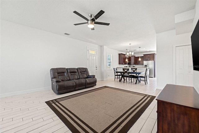 living room featuring baseboards, visible vents, light wood finished floors, and ceiling fan with notable chandelier