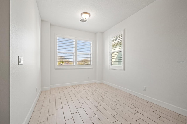 empty room with light wood finished floors, baseboards, visible vents, and a textured ceiling