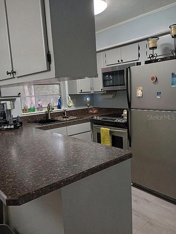 kitchen featuring stainless steel appliances, ornamental molding, white cabinets, a sink, and a peninsula