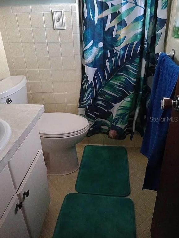 bathroom featuring toilet, a shower with curtain, tile walls, and vanity