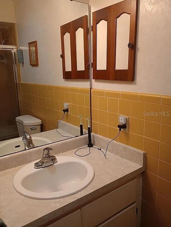 full bath with toilet, a stall shower, vanity, and tile walls