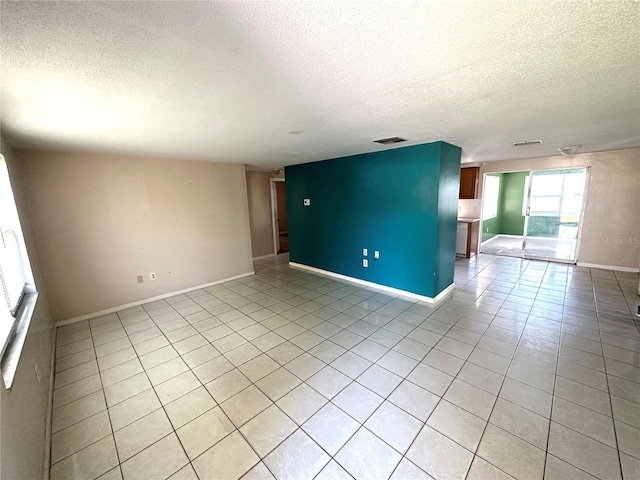 empty room featuring visible vents, a textured ceiling, baseboards, and light tile patterned floors