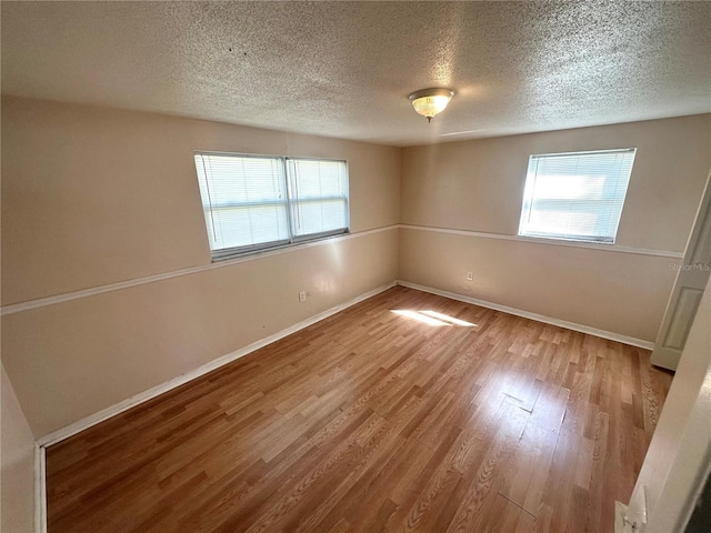 spare room featuring a textured ceiling, baseboards, and wood finished floors