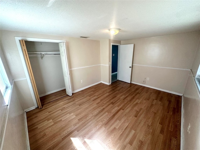 unfurnished bedroom featuring a textured ceiling, wood finished floors, visible vents, baseboards, and a closet