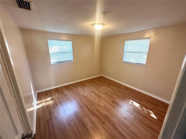 empty room with baseboards, plenty of natural light, visible vents, and wood finished floors