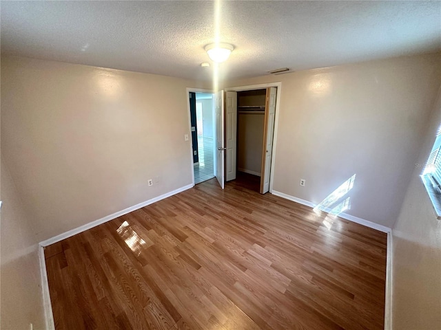 unfurnished bedroom featuring light wood-type flooring, a closet, baseboards, and a textured ceiling