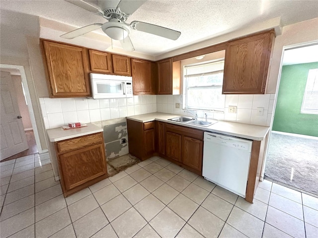 kitchen with white appliances, tasteful backsplash, light tile patterned floors, brown cabinetry, and a sink