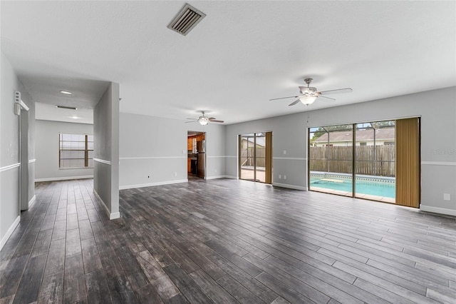 unfurnished living room with a ceiling fan, dark wood finished floors, visible vents, and baseboards