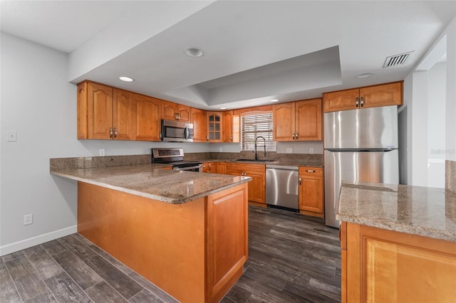 kitchen featuring appliances with stainless steel finishes, a raised ceiling, brown cabinets, and a sink