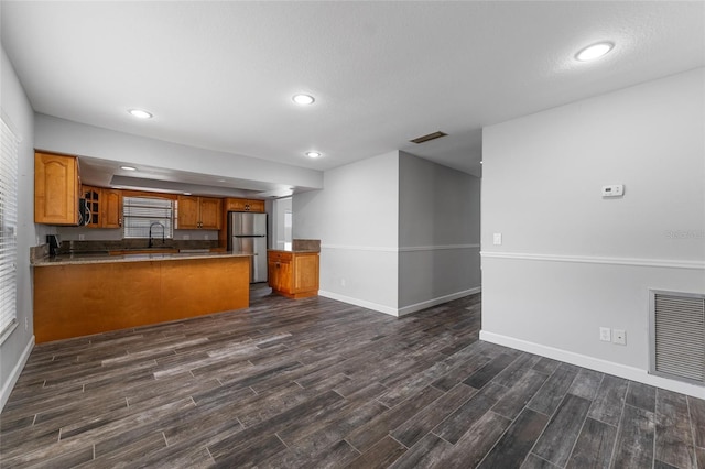 kitchen featuring dark wood-style flooring, brown cabinets, visible vents, freestanding refrigerator, and a peninsula