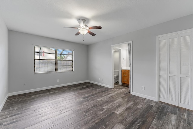 unfurnished bedroom featuring baseboards, ceiling fan, dark wood-type flooring, ensuite bathroom, and a closet