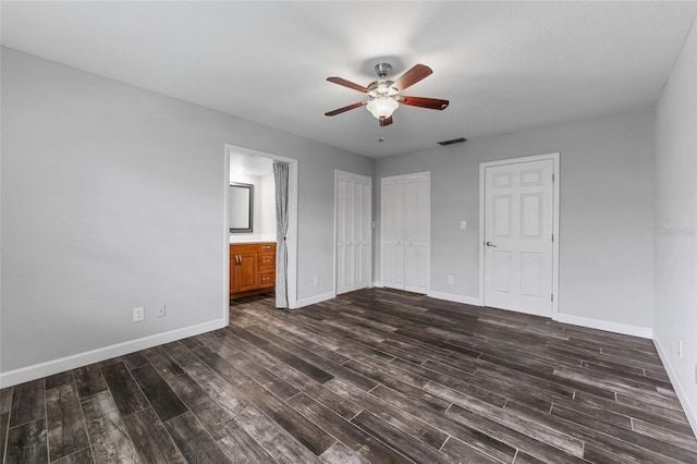 unfurnished bedroom with ceiling fan, connected bathroom, dark wood-type flooring, visible vents, and baseboards