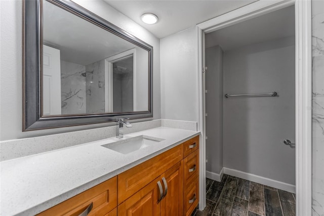 bathroom with wood finish floors, a marble finish shower, vanity, and baseboards