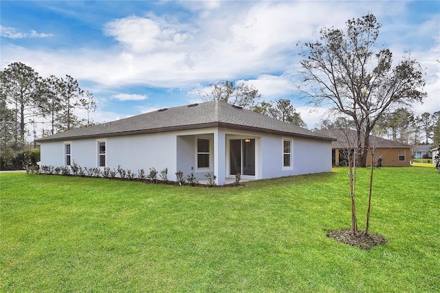 rear view of property featuring stucco siding, a shingled roof, and a yard