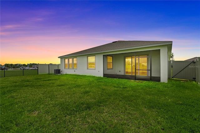 back of property at dusk featuring a yard, stucco siding, a gate, central AC, and fence