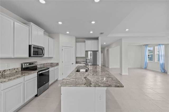 kitchen featuring a center island with sink, light stone counters, stainless steel appliances, a sink, and recessed lighting