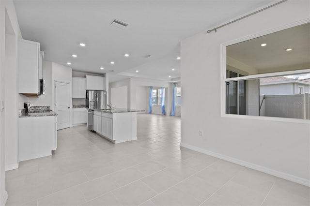 kitchen featuring light stone counters, visible vents, white cabinets, open floor plan, and a center island with sink