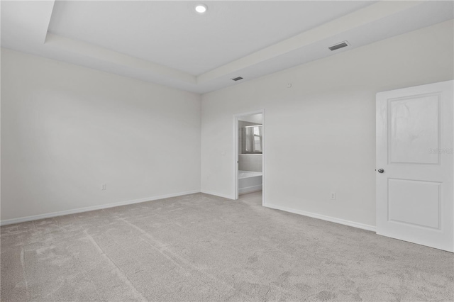 empty room with carpet, a raised ceiling, visible vents, and baseboards