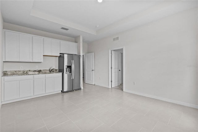 kitchen with light stone counters, visible vents, stainless steel refrigerator with ice dispenser, and baseboards