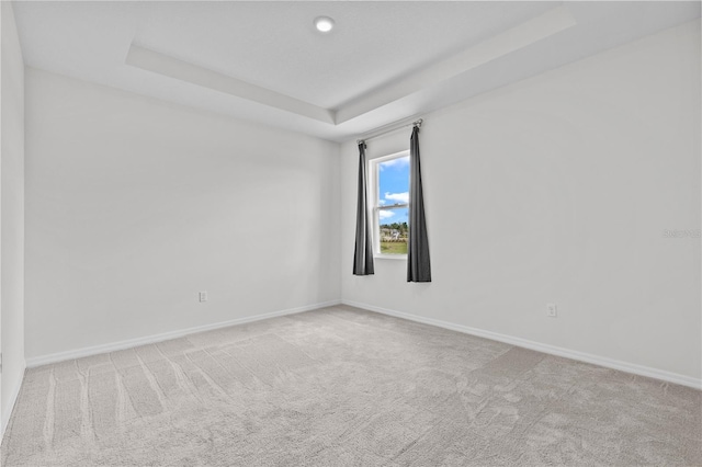 carpeted spare room featuring baseboards and a tray ceiling