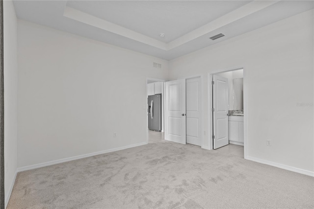 unfurnished bedroom with light colored carpet, a raised ceiling, visible vents, and stainless steel fridge with ice dispenser