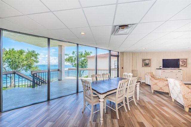 dining area featuring a water view, visible vents, a wall of windows, and wood finished floors